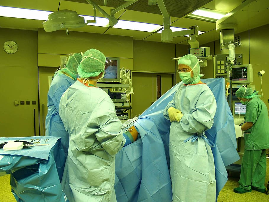 three people standing beside patient lying on bed inside operating room