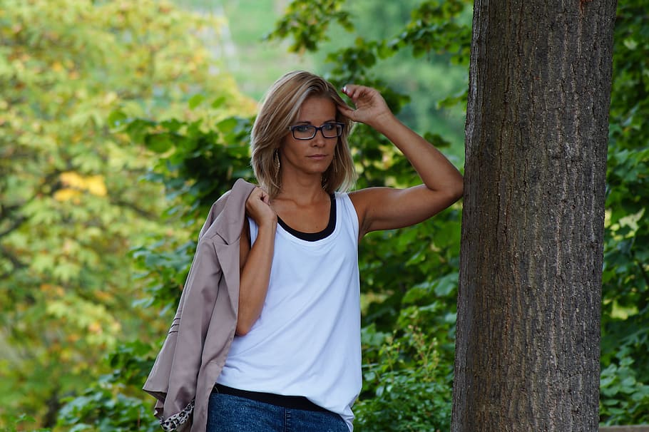 woman in white tank top standing and leaning on tree during daytime photography HD wallpaper