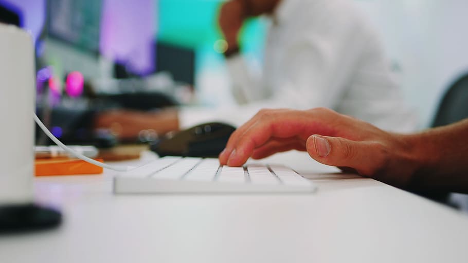 person holding white wireless computer keyboard on white wooden table inside room, shallow focus photography of persons hand on keyboard HD wallpaper