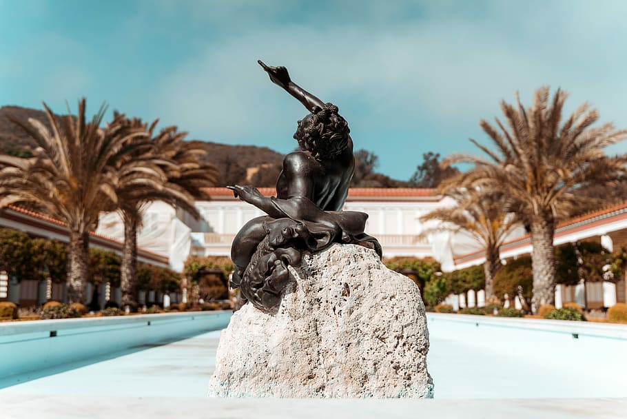 statue pointing upward, selective focus photography of woman in dress sitting on rock figurine HD wallpaper