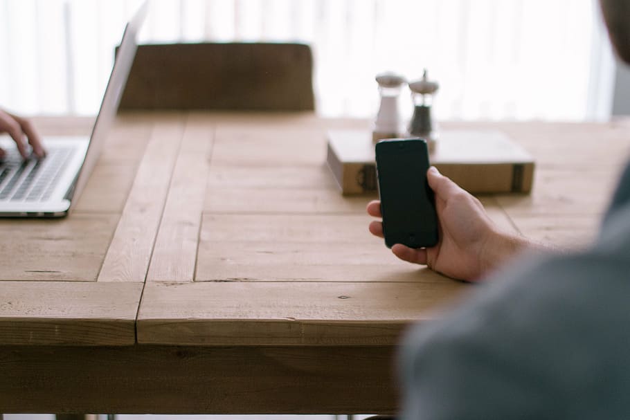 person holding smartphone on desk, black, leaning, brown, wooden HD wallpaper