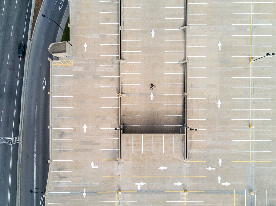 person lying on gray concrete parking area in aerial photography, gray concrete road beside brown concrete building HD wallpaper