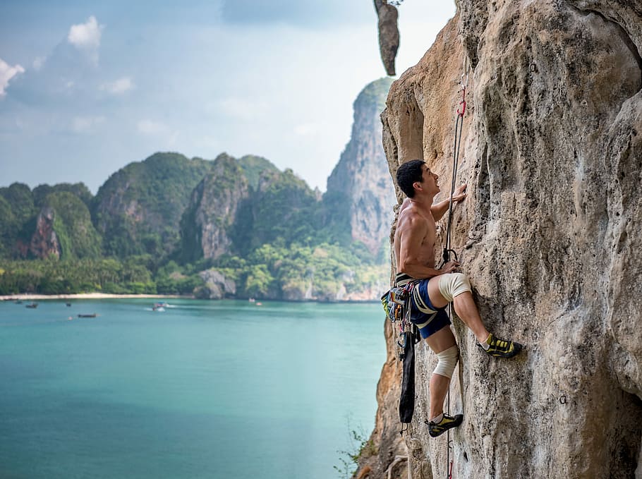 man wearing brown shirt mountain climbing at daytime, man in black and white shorts climbing cliff during daytime, HD wallpaper