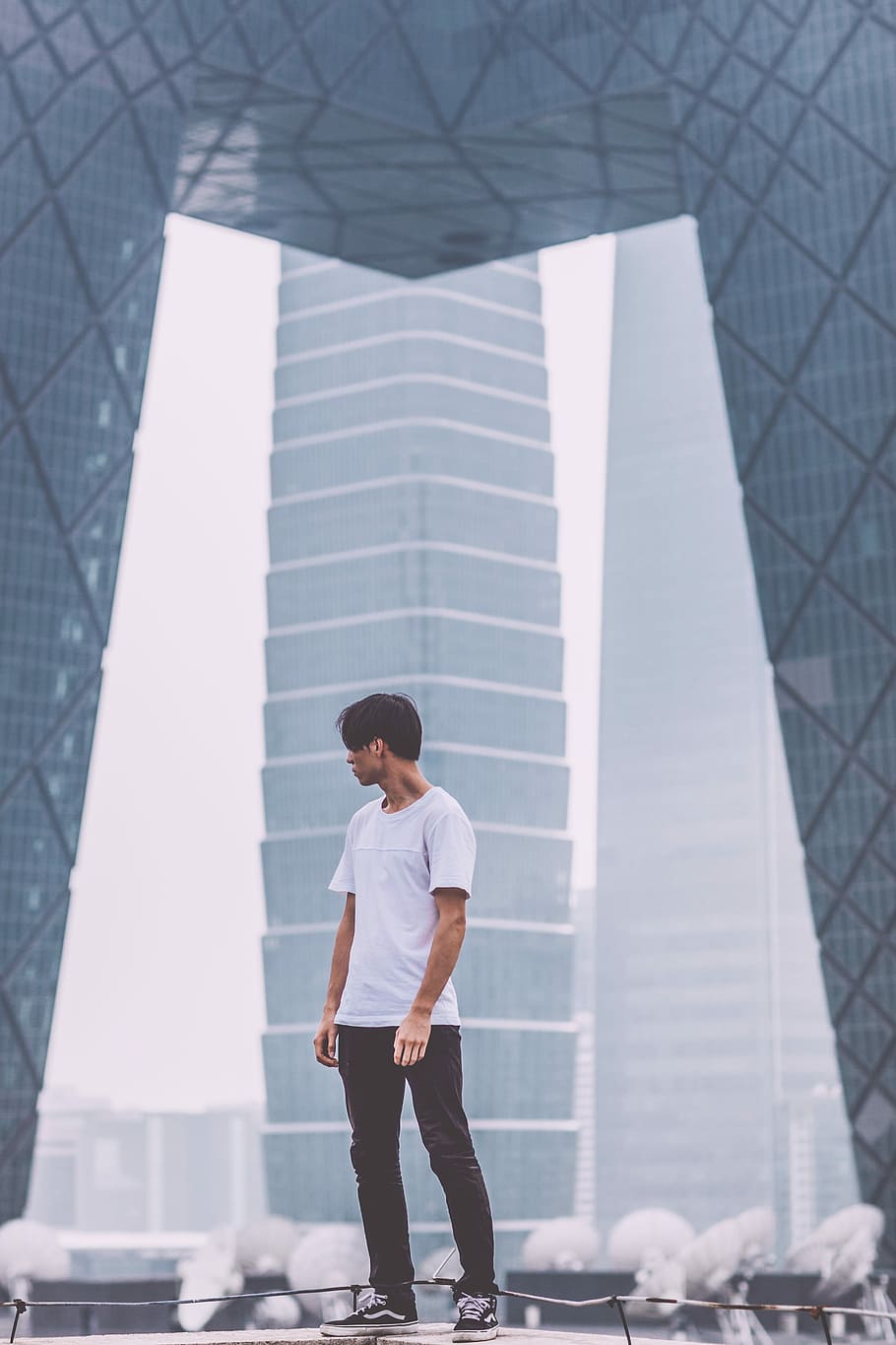 man wearing white crew-neck shirt standing near the building, man standing near concrete building during daytime HD wallpaper