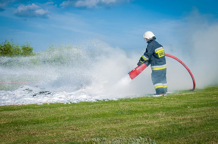 man holding red fire extinguisher on green grass field during daytime HD wallpaper