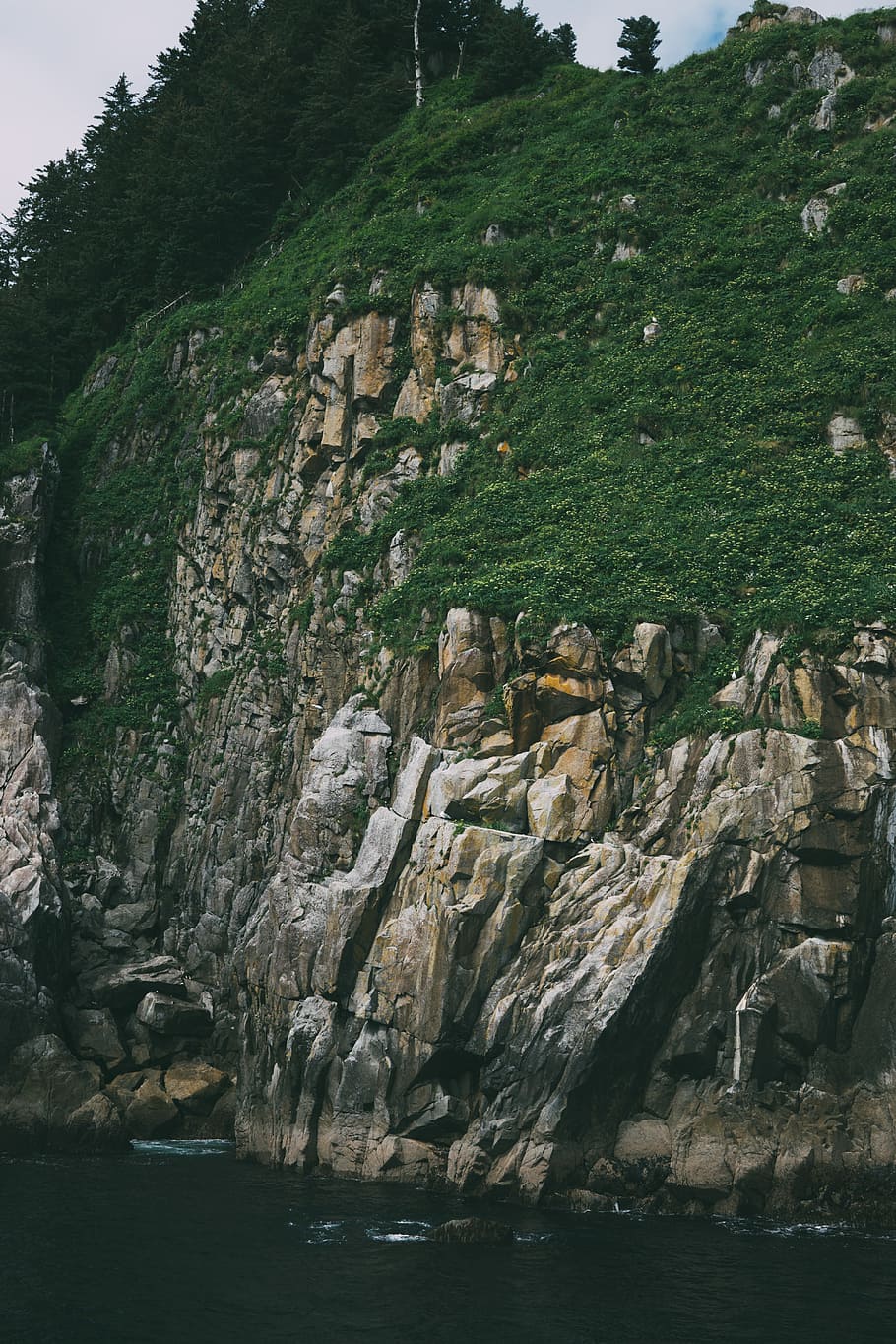 rock formation beside body of water during daytime, brown rock formation surrounded by green plants and trees HD wallpaper