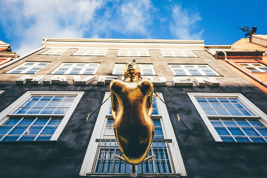 low angle photography of brown woman statue in front of building under white and blue building, low-angle photography of bronze statue on side of building near window HD wallpaper