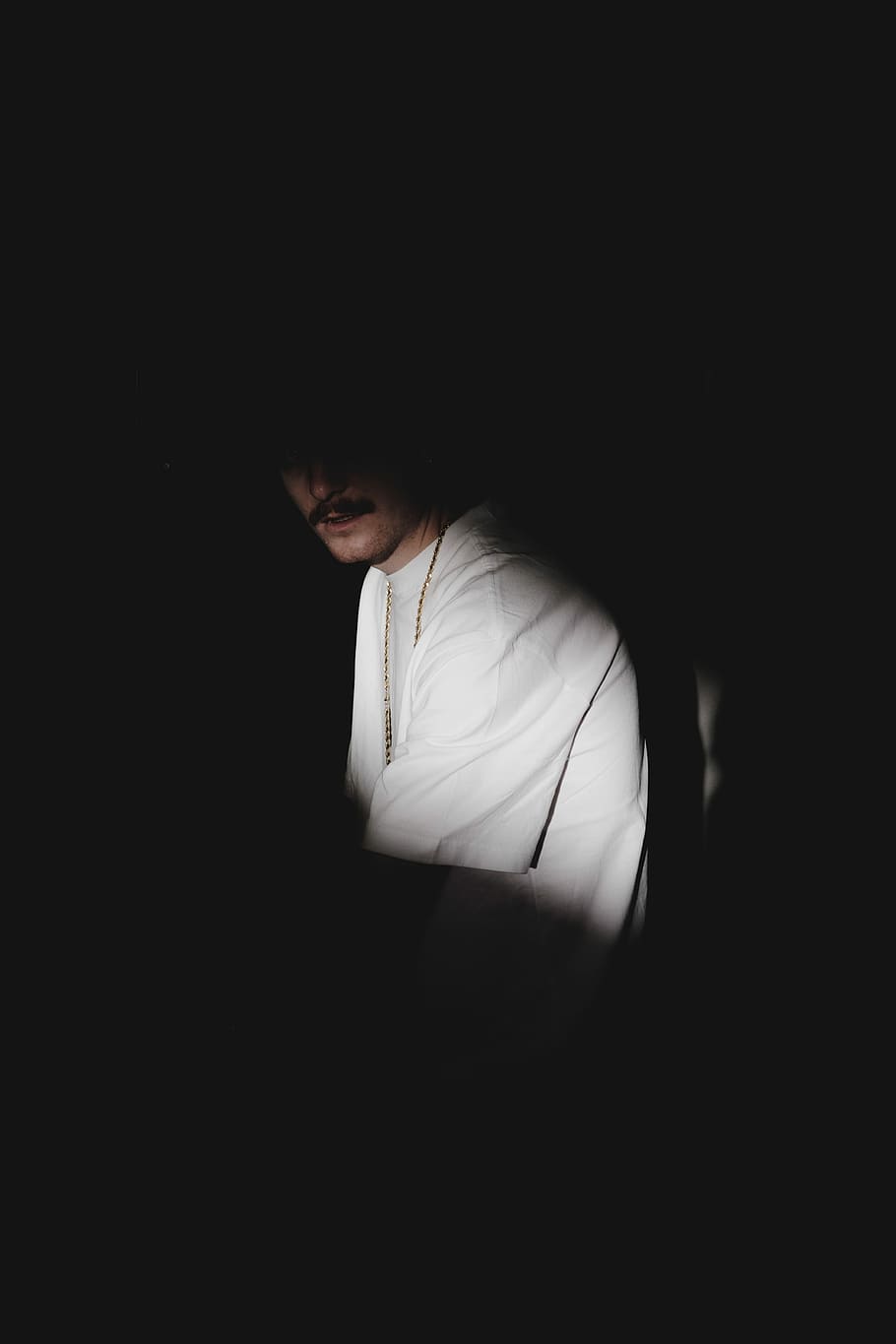 man wearing white top, man in the dark shadows, person, moustache