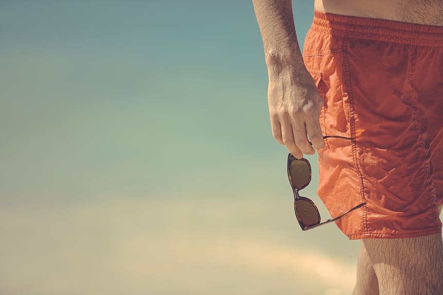 man holding sunglasses on seashore, beach, red, shorts, bermudas HD wallpaper