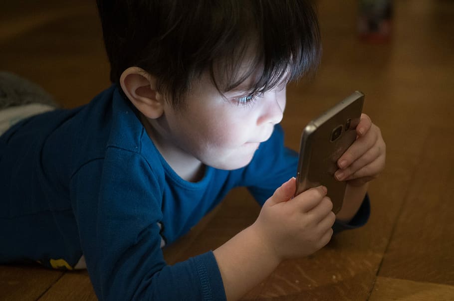 boy staring at Samsung smartphone while leaning on floor, mobile phone