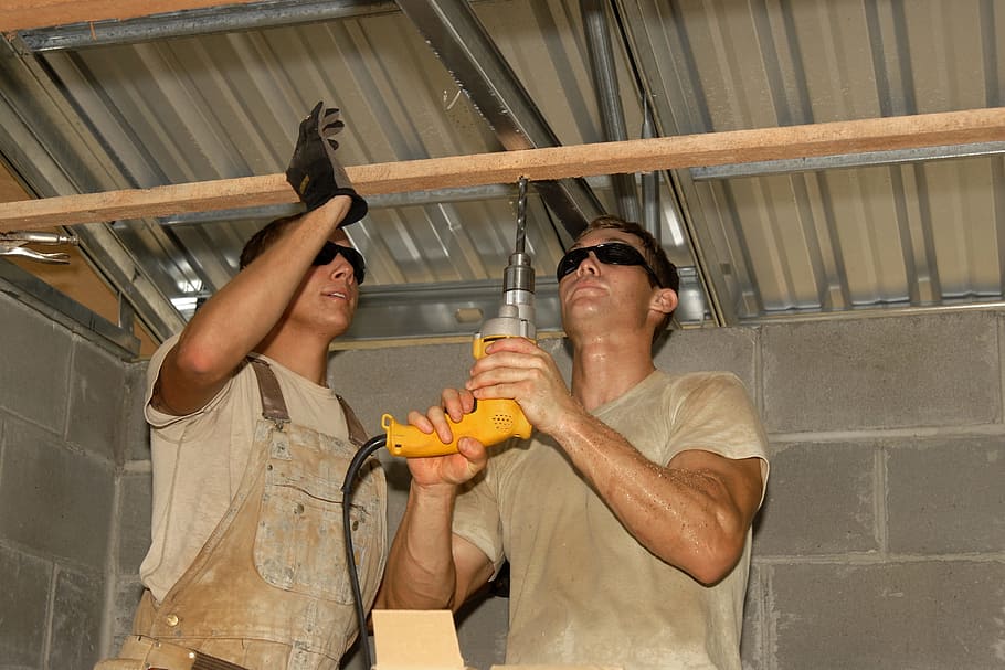 man wearing gray crew-neck t-shirt using yellow corded hand drill HD wallpaper