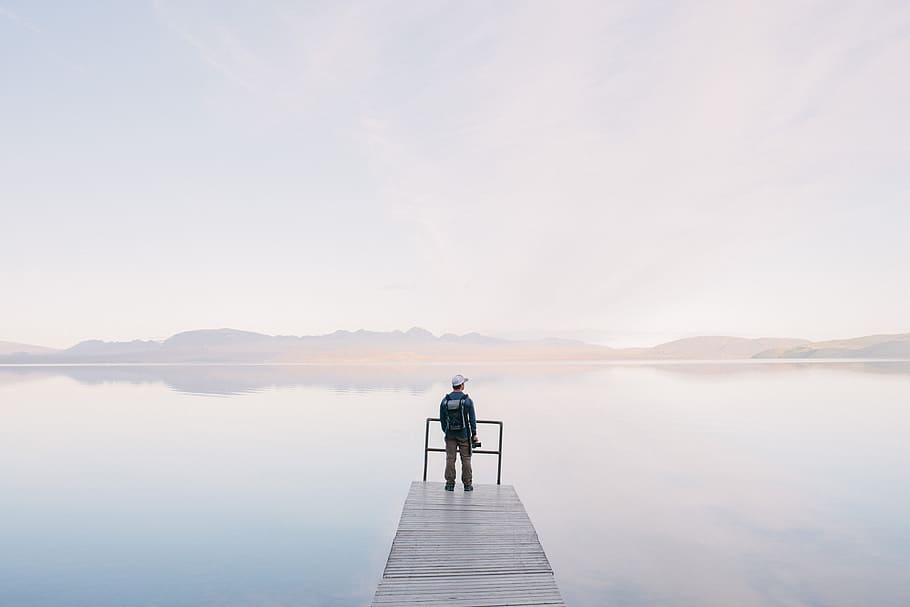 Man Wearing Jacket Standing on Wooden Docks Leading to Body of Water HD wallpaper