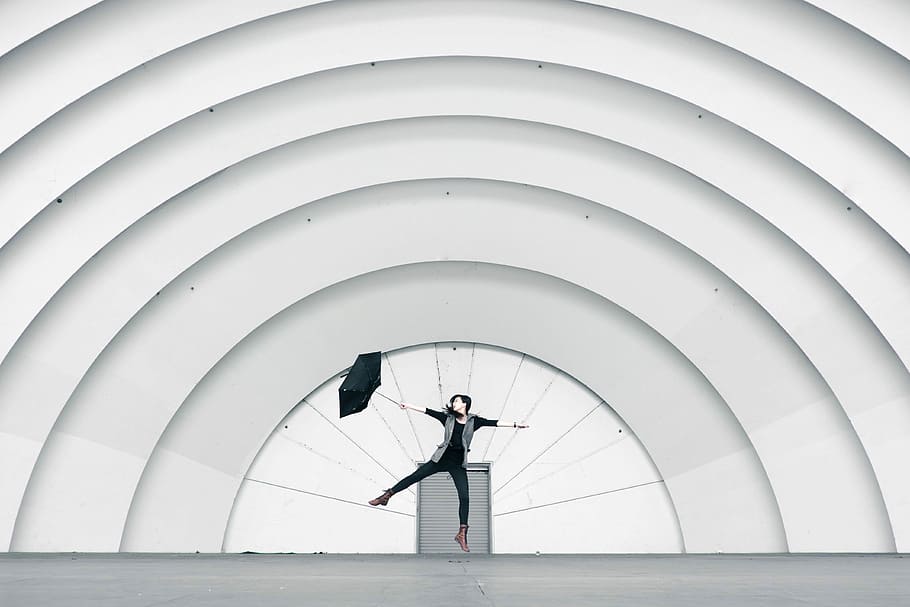 woman standing on stage, woman holding umbrella jumping near roller shutter HD wallpaper