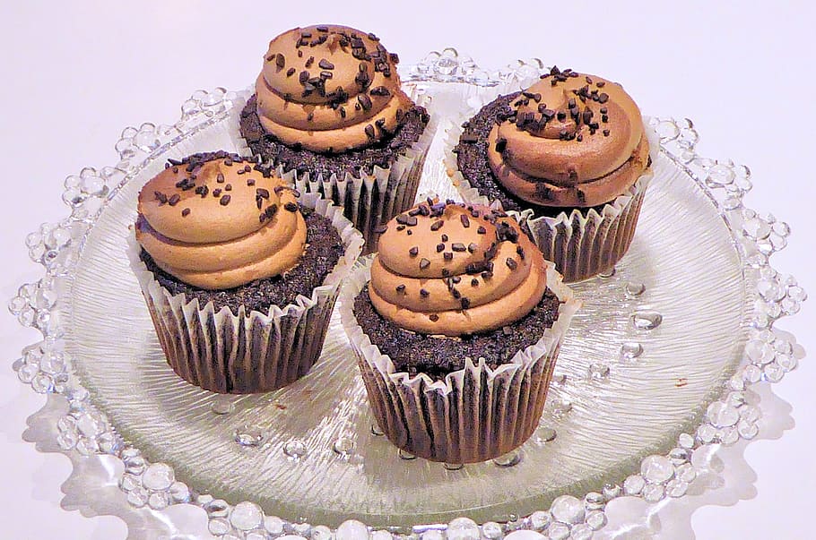 four black-and-brown cupcakes on glass tray, chocolate cupcakes