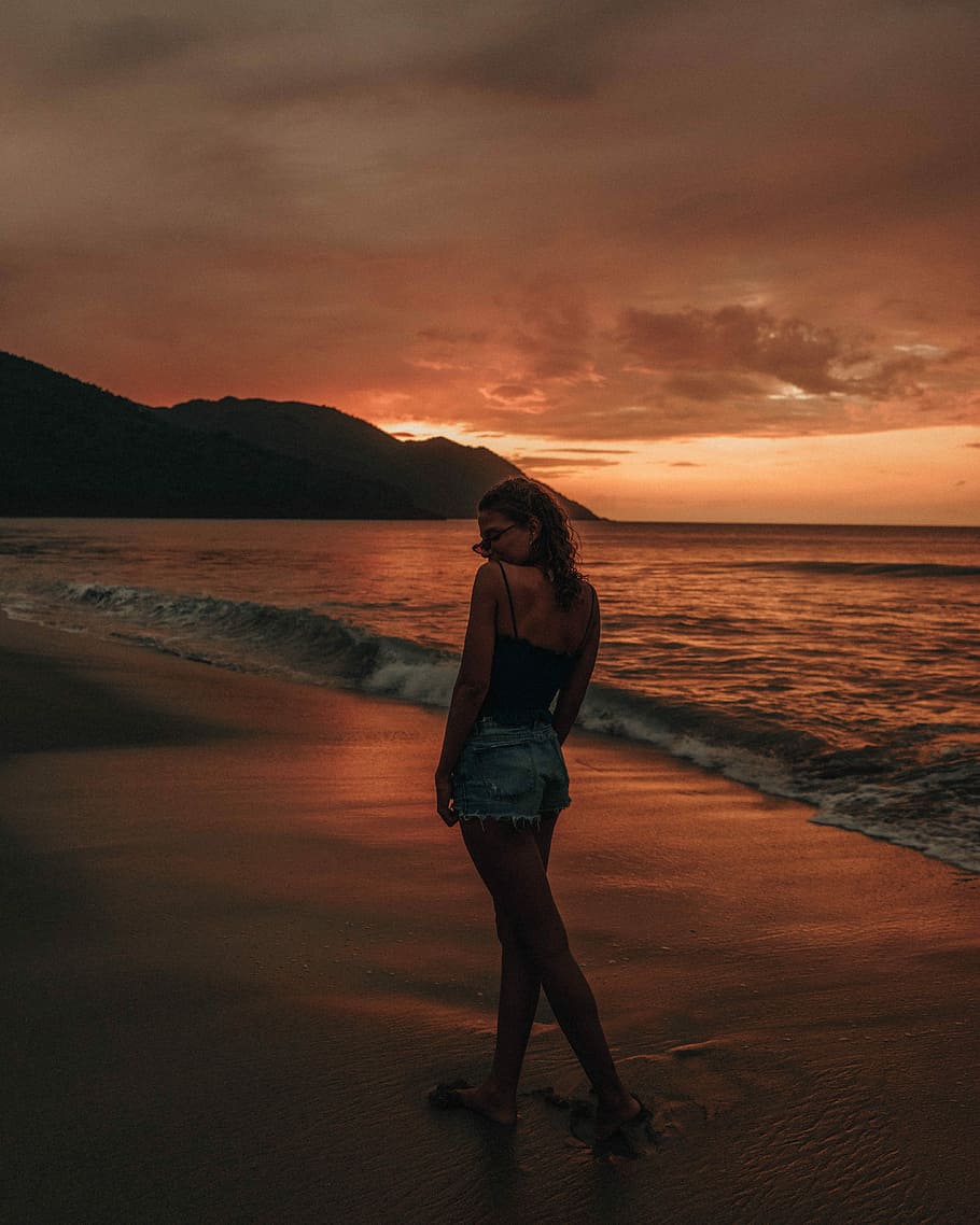 woman standing on sea shore, woman walking on the shore during sunset HD wallpaper