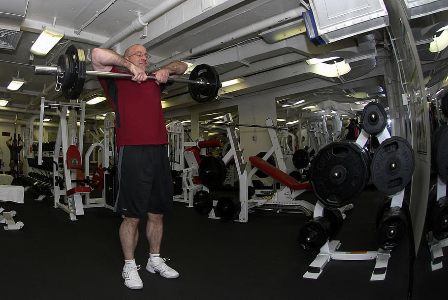 man carrying silver and black barbell inside the gym, gym room