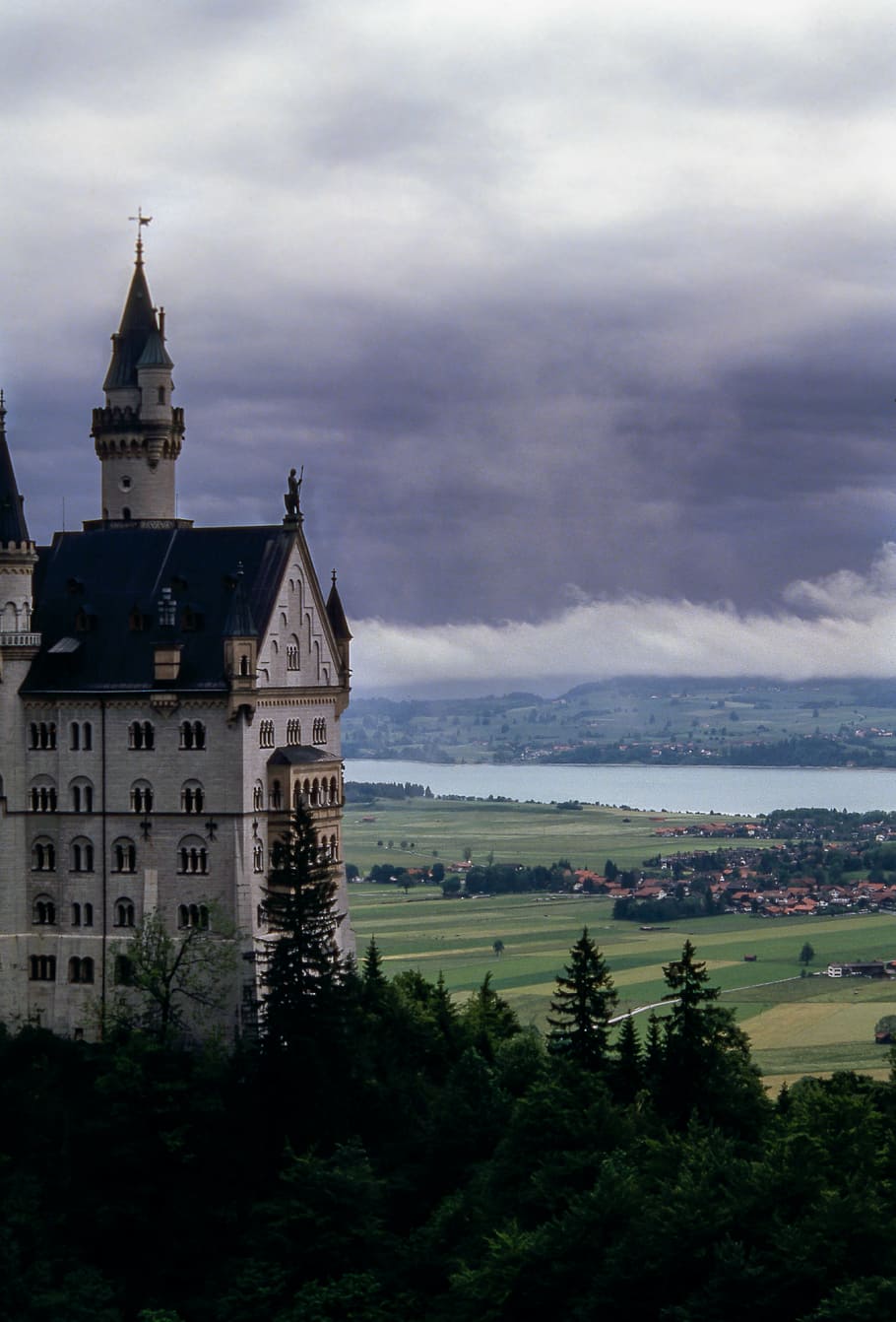 brown building near field and body of water during cloudy day HD wallpaper