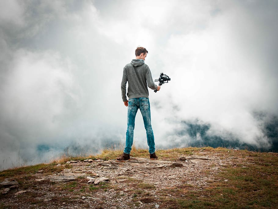 man holding camera with stabilizer while standing, man holding camera stabilizer facing on cumulus clouds HD wallpaper