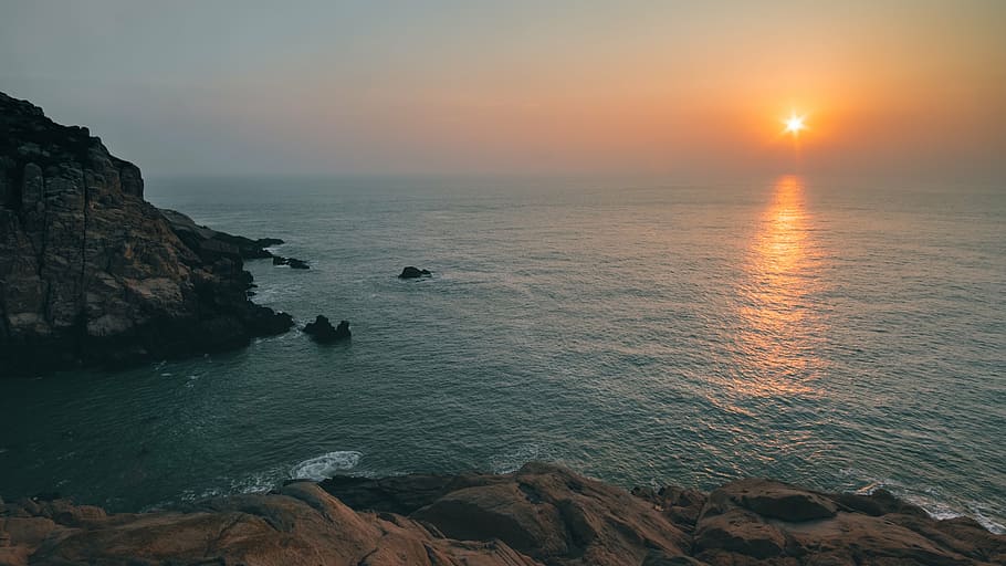 calm body of water and brown rock formation during golden hour HD wallpaper