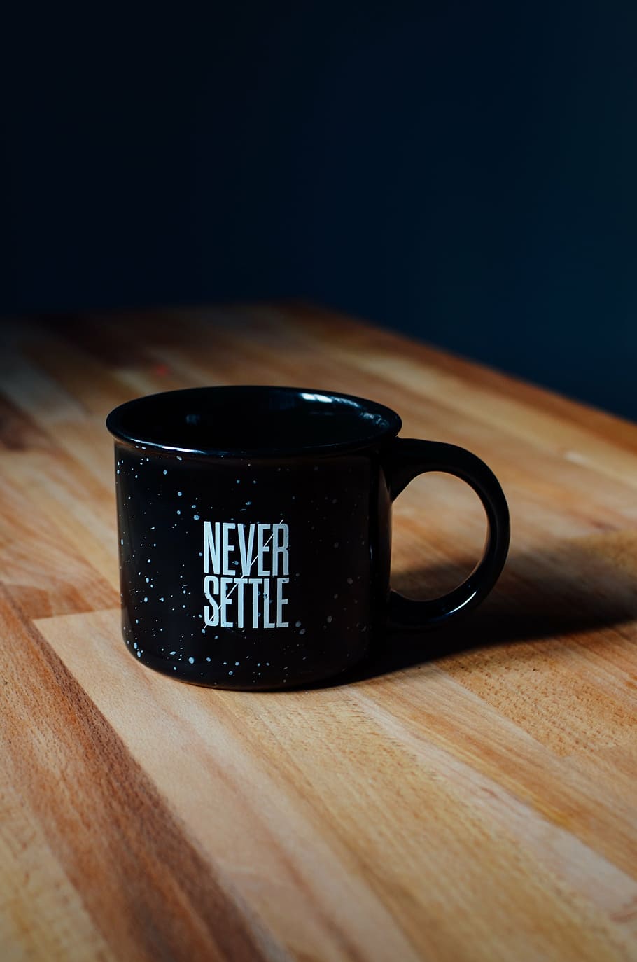 black Never Settle ceramic mug on brown wooden table, quote, statement