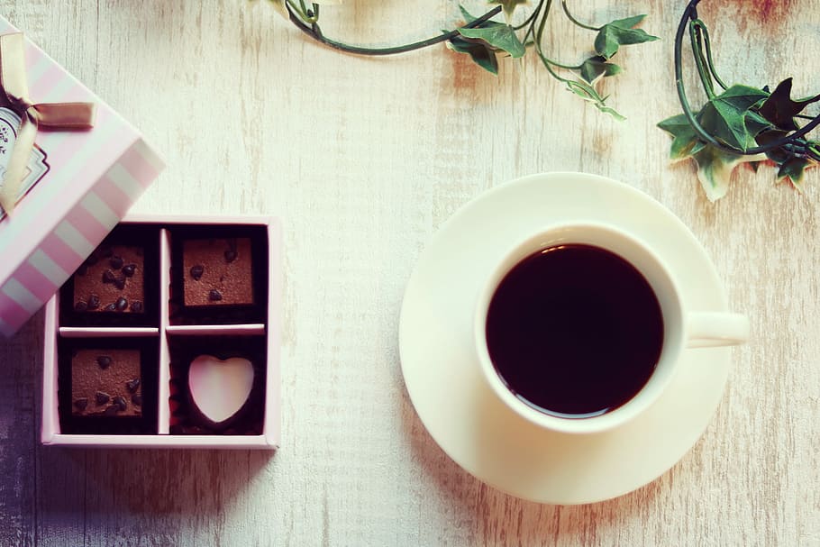 white ceramic cup with saucer and black coffee near chocolates HD wallpaper