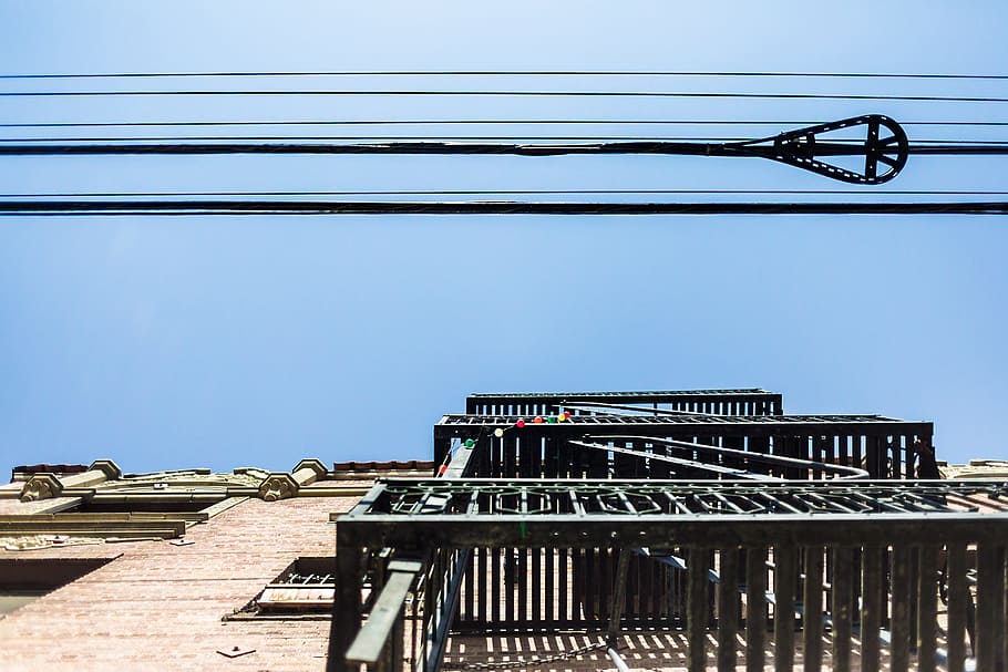gray metal frames under black cables at daytime, worm view of building under blue sky