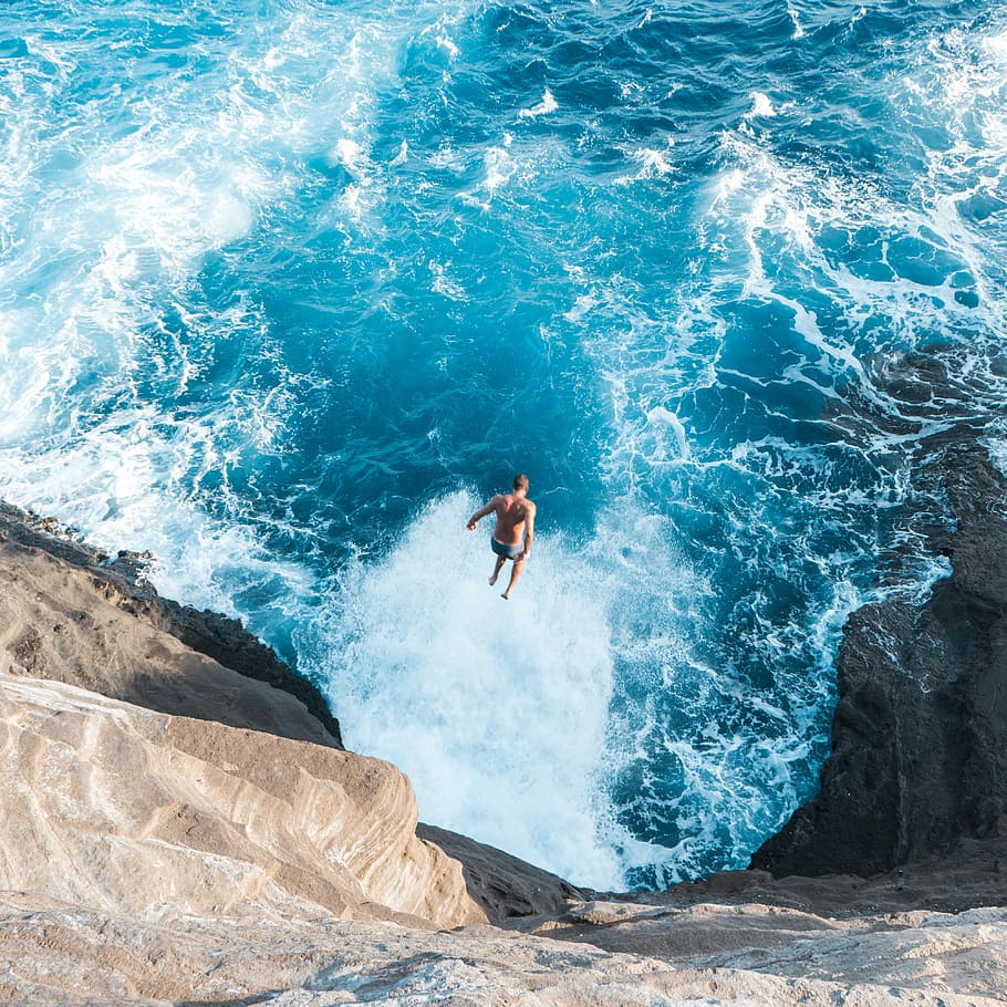 aerial photo of man jumping on cliff to the water, man jumping in to blue body of water