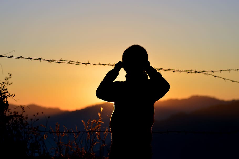 Silhouette of Boy Standing Near Barbed Wire, afterglow, backlit