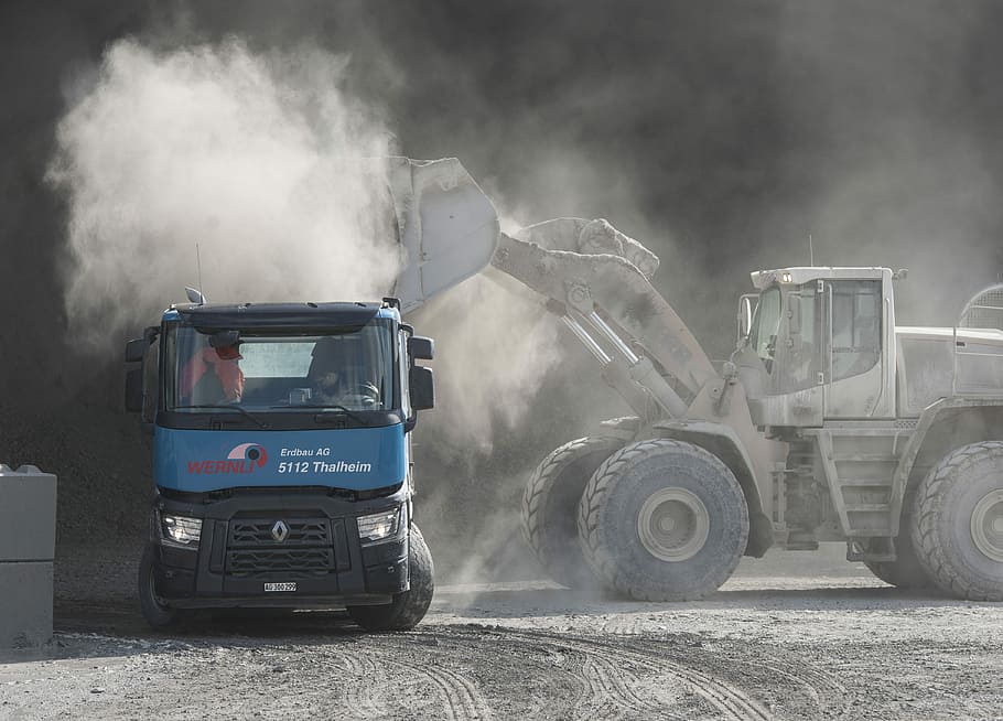 grey front loader loading sand on blue dump truck during daytime