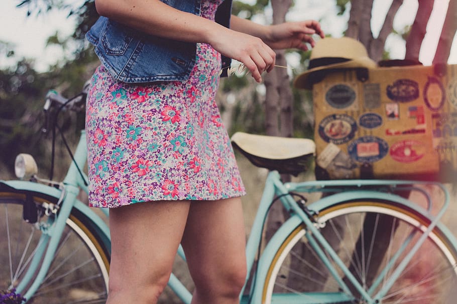women in front of teal step-through bicycle, woman wearing blue denim top and floral multicolored mini dress standing near teal bicycle