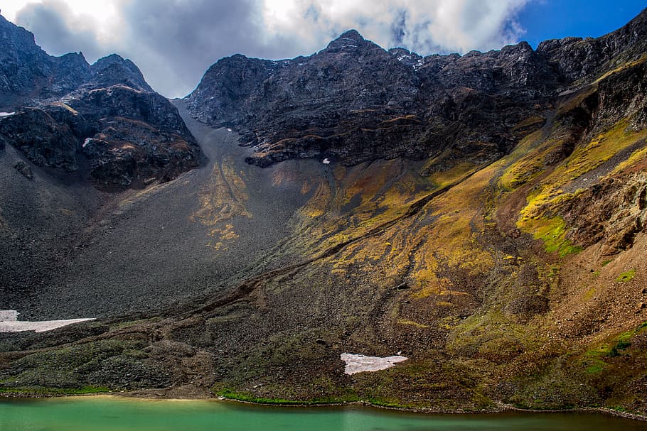 mountain surrounded with clouds, brown cliff near body of water under cloudy sky HD wallpaper