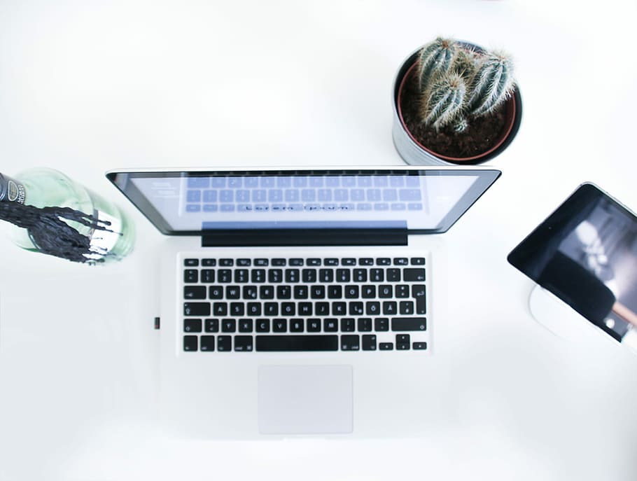 An up-top view of a laptop sitting on a white desk., MacBook Pro on white table beside succulent plant and green glass bottle