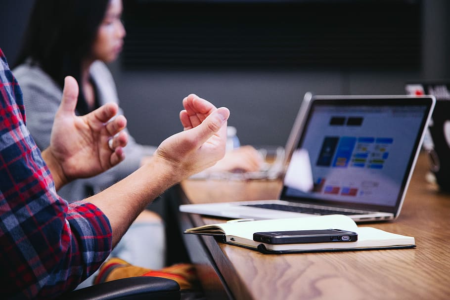 black smartphone near person, selective focus photography of person in red shirt doing hand gesture in front of brown table HD wallpaper