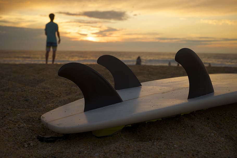 white and black surfboard on sand near seashore at golden hour HD wallpaper