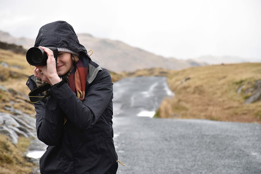 woman holding camera standing on gray concrete road at day time HD wallpaper