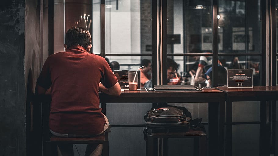 man sitting on brown wooden bar stool beside backpack on wooden bar stool, person sitting on brown bar stool HD wallpaper