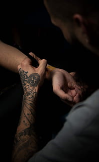 man's tattooing person's hand, man in gray shirt doing henna tattoo on person's right wrist HD wallpaper