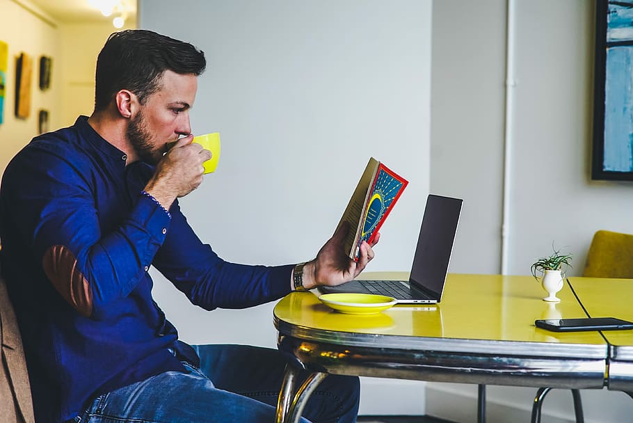 man drinking on yellow cup while reading book, man holding cup and reading book HD wallpaper