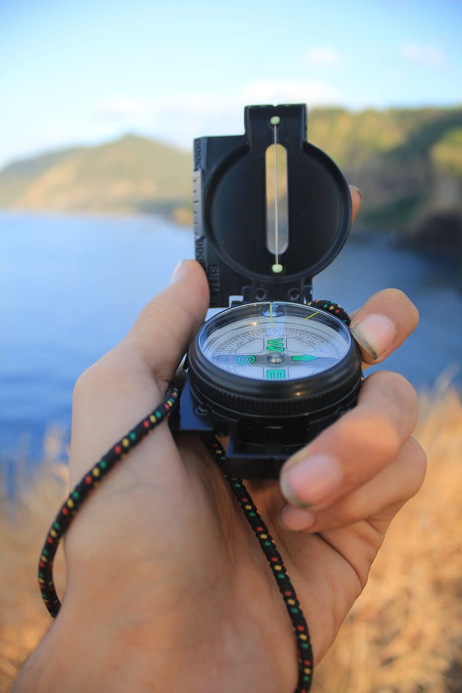 person holding black compass in front of ocean water during daytime shallow focus photography