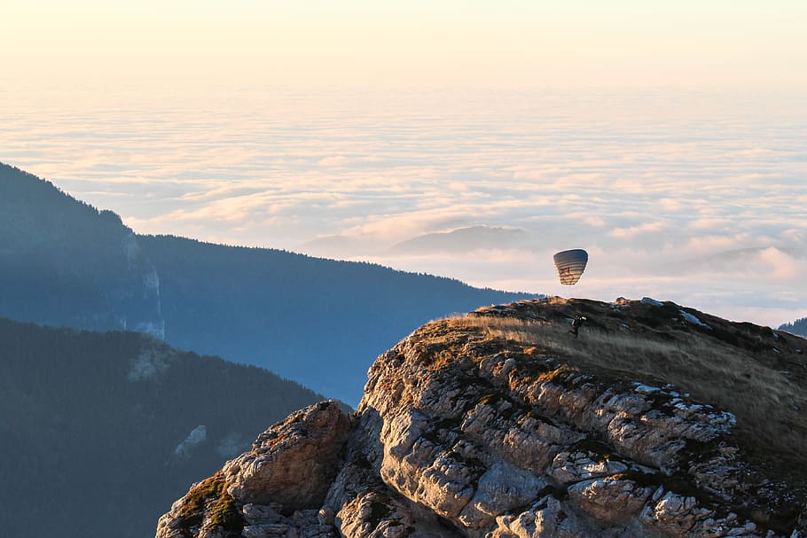 person riding parachute on mountain top, brown mountain cliff HD wallpaper