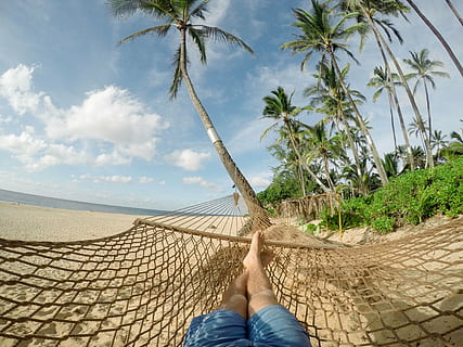person with blue shorts lying on brown mesh hammock on seashore with blue sky and white clouds during daytime close-up photography HD wallpaper