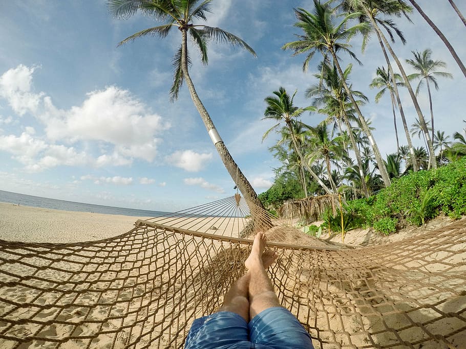 person with blue shorts lying on brown mesh hammock on seashore with blue sky and white clouds during daytime close-up photography HD wallpaper