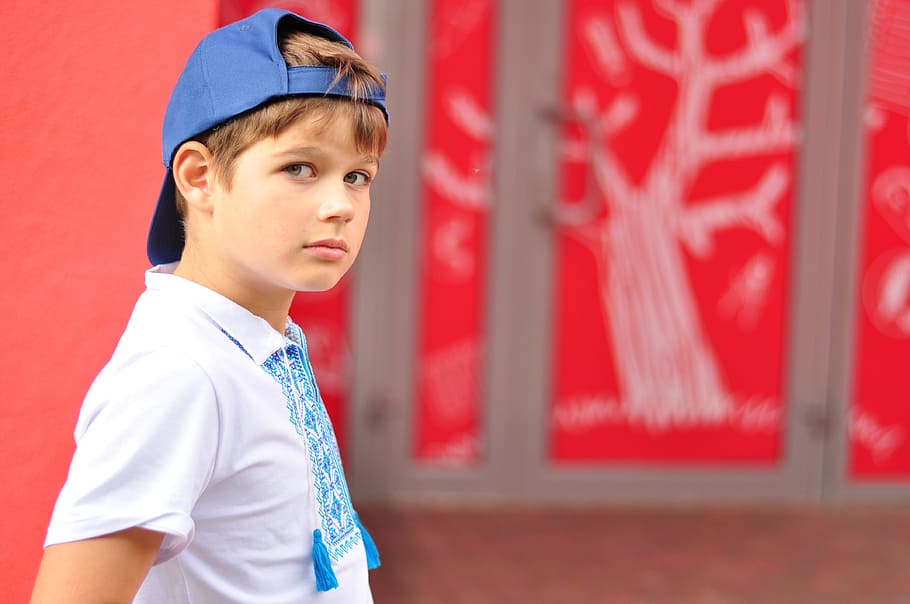 boy wearing blue fitted cap backwards near red wall, Schoolboy