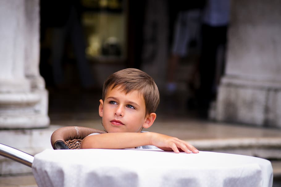 boy looking sideways while sitting on brown chair outdoors, toddler sitting in front of table HD wallpaper
