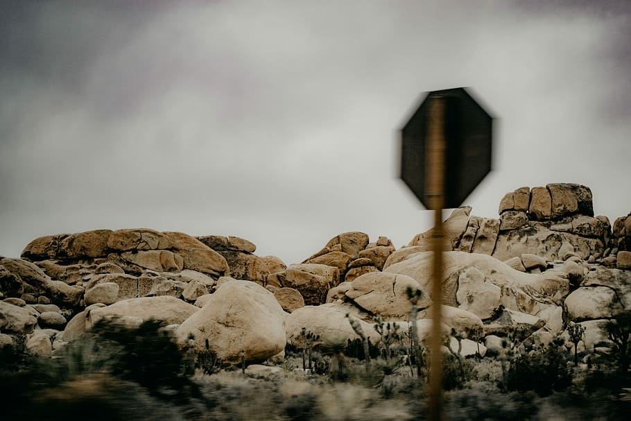signage near rock formation, brown rocks near plants under cloudy sky during daytime HD wallpaper
