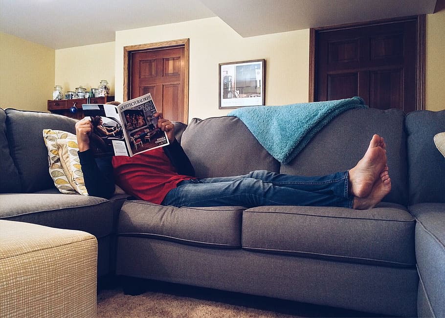 man reading book while lying on gray couch, home, life, sofa HD wallpaper
