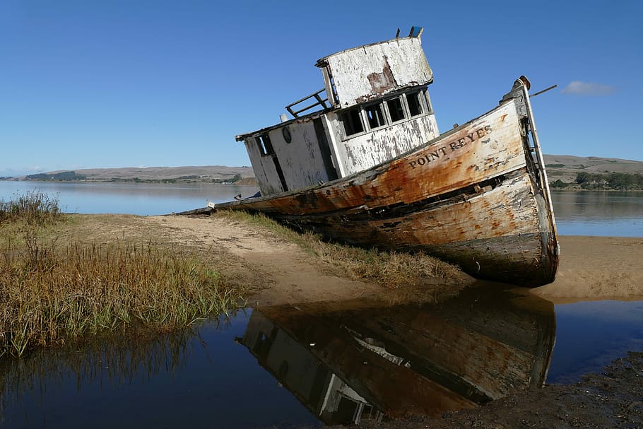 brown-and-white boat on land, abandoned boat leaning on soil near lake during clear blue sky HD wallpaper
