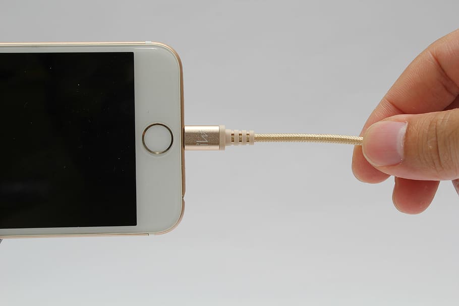 person holding brown lightning cable connected to gold iPhone 6 with turned-off screen HD wallpaper