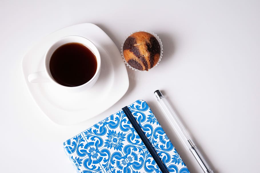 white ceramic cup with coffee, black pen near blue book and filled teacup HD wallpaper