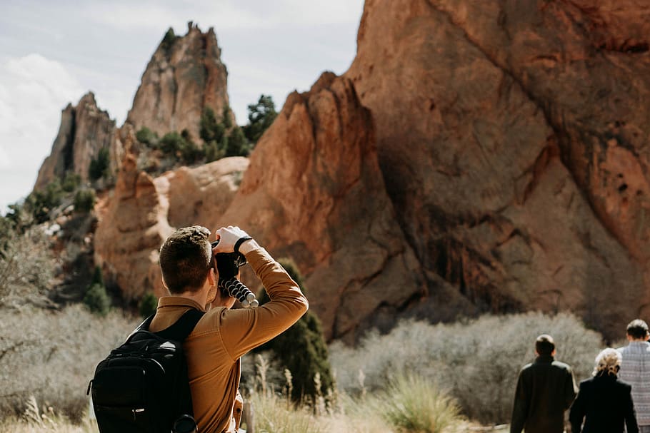 man taking photo of rock formation, man in brown dress shirt using DSLR camera